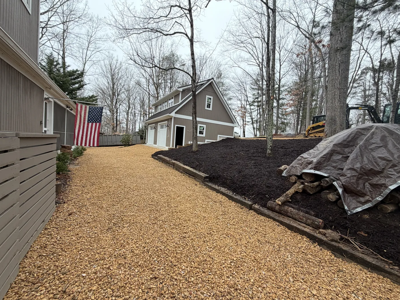 Front view of garage with gravel driveway through wooded lot