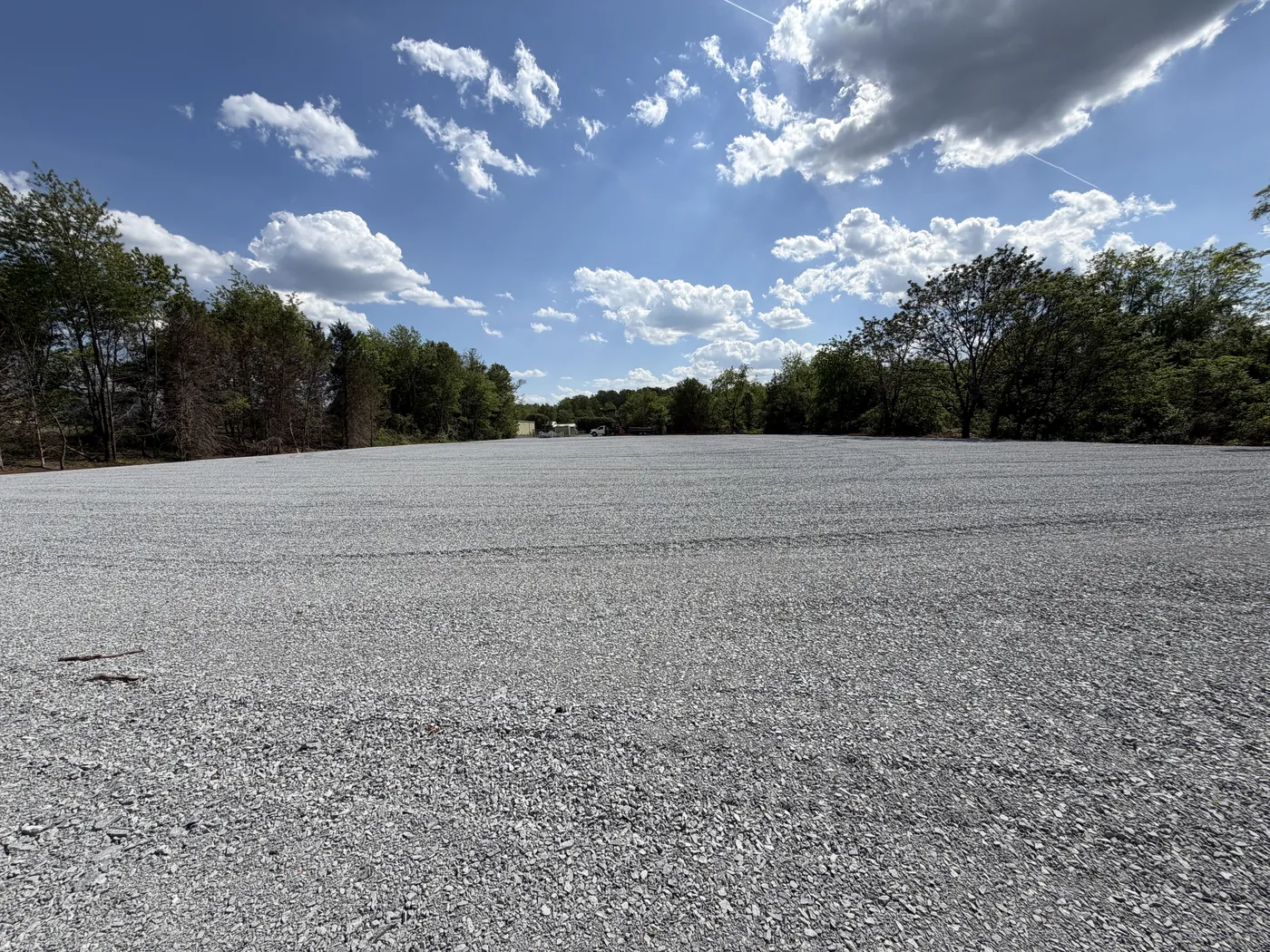 Expansive crushed stone commercial lot with treeline backdrop